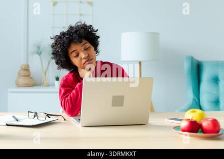 Sleepy sad African American woman sitting at table with laptop. Tired overworked girl lazy to work. Student businesswoman relaxi Stock Photo