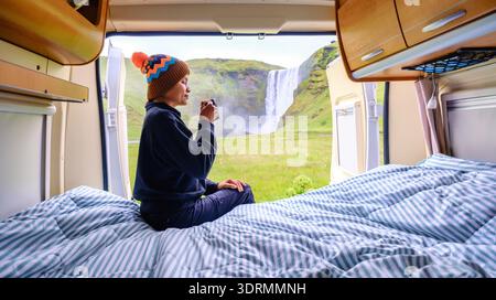Asian woman drinking coffee in a campervan by the waterfall, Skogafoss waterfall, Iceland. Stock Photo
