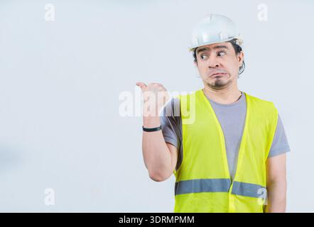 Funny construction worker pointing at an isolated blank space. Surprised builder pointing at an isolated advertising space Stock Photo