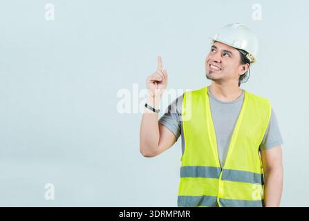 Smiling engineer pointing up isolated. Happy young builder with helmet pointing up Stock Photo