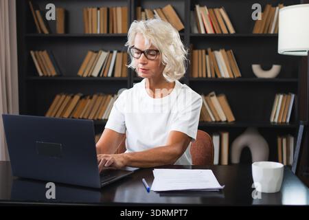 Confident stylish middle aged senior woman using laptop at workplace. Older mature lady businesswoman sitting at office table wi Stock Photo