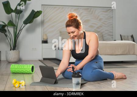 Yoga fitness workout training online. Woman practicing stretching with online app lessons at home. Plus size female doing sports Stock Photo