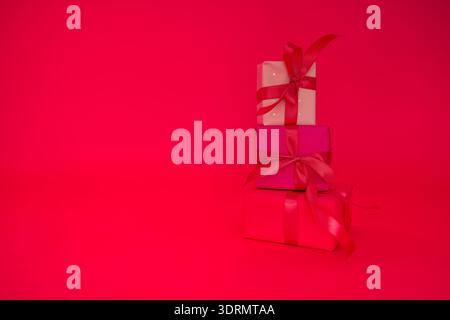 Three gifts in a bright package with satin bows on a pink background. Festive boxes with pink ribbons on an isolated backdrop. Stock Photo