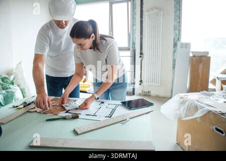 Male construction worker and female architect collaborating on building plans at a table in a renovation site, showcasing teamwo Stock Photo