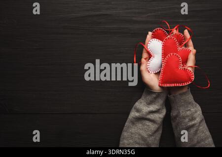 Hands Holding a Collection of Red and White Fabric Hearts on a Black Wooden Surface Stock Photo