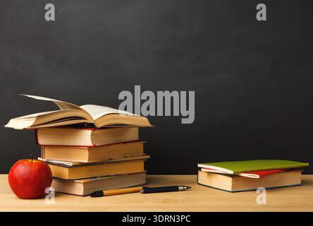Collection of Books and an Apple on a Table in a Classroom Setting Ready for Reading Stock Photo