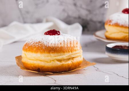 Delicious jam donuts in powdered sugar on parchment paper on the table Stock Photo