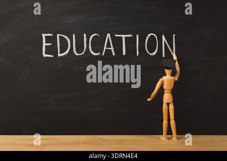 Wooden Figure Writes Education on Chalkboard in Classroom Setting During Daylight Stock Photo