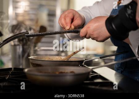 Close up of chef grating nut over pan on stove. Stock Photo