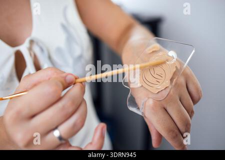 Female makeup artist applying foundation on hand using a spatula, showcasing skin tone matching techniques and beauty applicatio Stock Photo