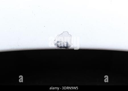 Car Paint Damage Repair, A close-up view shows a small area of chipped and peeling white paint on a car fender, revealing the dark metal substrate. Stock Photo