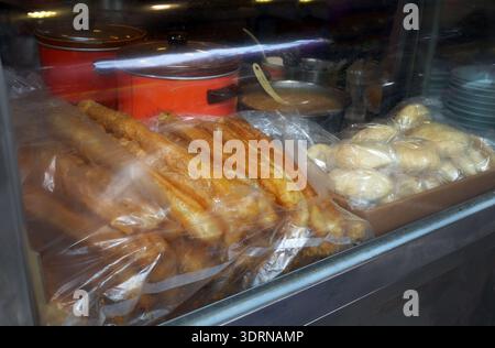 Freshly fried Youtiao dough sticks and round pastries packed in clear plastic bags, ready for takeaway at Taiwan breakfast stall. The popular street f Stock Photo