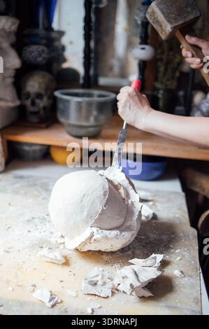 Skilled artisan using a hammer and chisel to sculpt a plaster mold on a workbench surrounded by artistic tools and materials, sh Stock Photo
