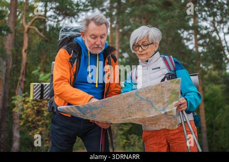 Hiking tourism. Senior couple man woman looking track in paper map enjoying hiking in forest. Happy old people backpackers hiker Stock Photo