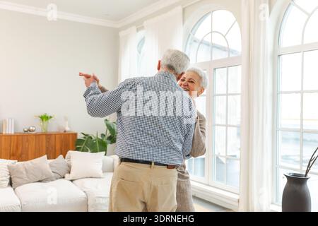 Keep moving. Romantic senior mature couple dancing to music together at home. Happy smiling family retired man woman husband wif Stock Photo