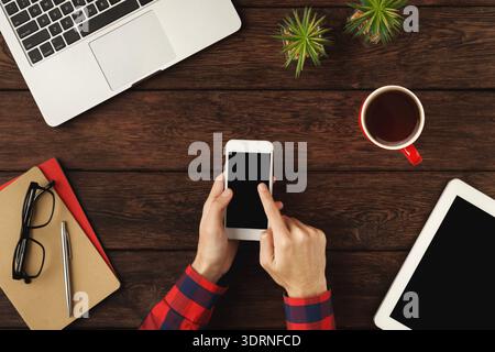 Collection of Devices and Materials on a Wooden Table With an Individual Using a Smartphone Stock Photo