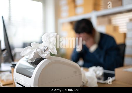 Label printer malfunction on work desk while stressed warehouse owner faces business problems Stock Photo