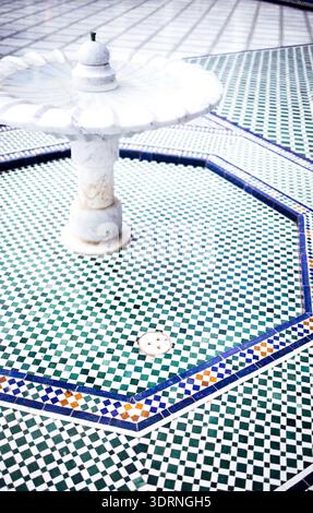 Ornate fountain in a tiled courtyard, featuring intricate geometric patterns in green and blue, surrounded by a tranquil atmosph Stock Photo