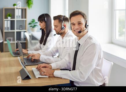 Smiling callcenter team using headsets and laptops while providing customer support Stock Photo