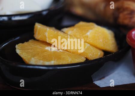 Sliced orange served on a black plate with pastries Stock Photo