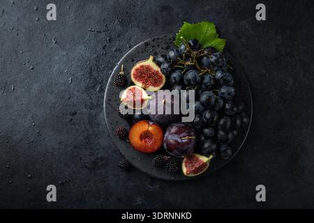 Fresh dark fruits on black plate, concrete background Stock Photo