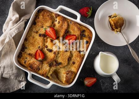 Bread and butter pudding with raisins and fresh strawberry in white baking dish Stock Photo