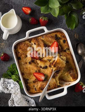 Bread and butter pudding with raisins and fresh strawberry in white baking dish Stock Photo