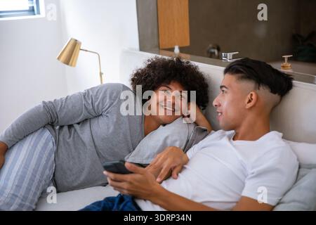 Diverse male friends lounging on sofa in home living area with striped pillow and smartphone. Coziness, relaxation, contemporary Stock Photo