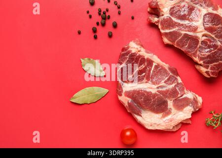 Fresh raw steaks with different spices and cherry tomato on red background Stock Photo