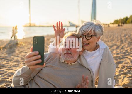 Video call. Senior couple making selfie having video call on beach outdoor. Mature old grandmother grandfather talking speaking Stock Photo