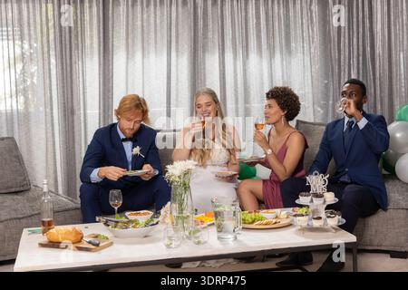 Diverse wedding party slicing bread and sipping wine at banquet lounge with cupcakes. Celebration, unity, elegance, festivity, c Stock Photo