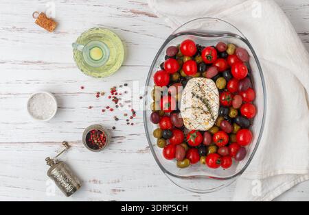 White cheese (camembert, brie) for baking with cherry tomatoes, black and green olives, kalamata, thyme and olive oil in a glass Stock Photo