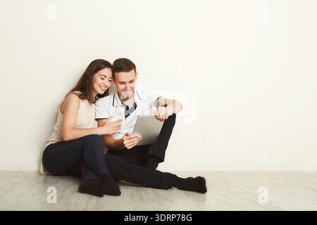 Couple Sitting on Floor Using Tablet and Enjoying Time Together in a Simple Indoor Space Stock Photo