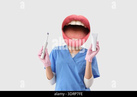 Female dentist with mouth instead of head holding electric tooth brush and paste on light background Stock Photo