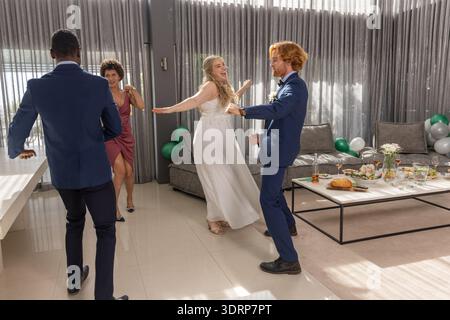 Diverse wedding party dancing in formal attire at wedding reception with coffee table and balloons. Celebration, joy, elegance, Stock Photo