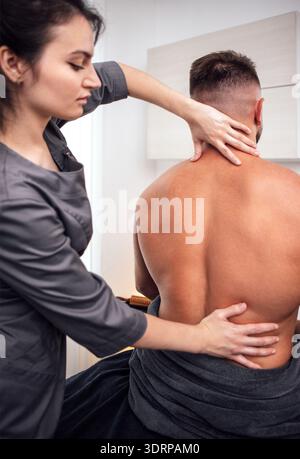 Female massage therapist providing a relaxing back massage to a male client in a serene spa environment, showcasing wellness and Stock Photo