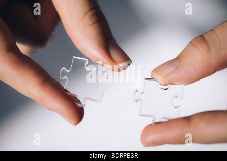 Two hands holding clear puzzle pieces, demonstrating the process of connecting them together, symbolizing problem-solving and co Stock Photo