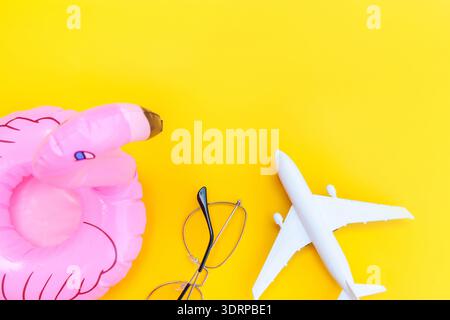 Summer beach composition. Minimal simple flat lay with plane sunglasses and Inflatable flamingo isolated on yellow background. V Stock Photo