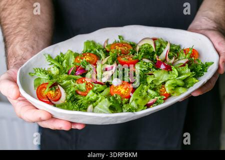 White plate with lettuce, cherry tomatoes and red onion salad with olive oil, mustard and wine vinegar dressing in men's hands. Stock Photo