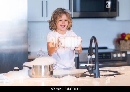 Boy washing dishes with bubbles. Child playing with foam in kitchen. C Funny boy enjoying house chores. Playful child washing kitchenware. Kid in soap Stock Photo