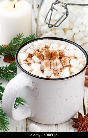 Hot cocoa (coffee or chocolate) with marshmallows and cinnamon in a white Cup. Candy, candles and fir branches on the table. Chr Stock Photo