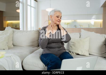 Middle aged senior woman at home relaxing stretching hands and body taking break from work on laptop. Older mature woman happy a Stock Photo