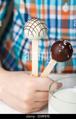 Two cake pops decorated with white and dark chocolate in children's hands. Dessert for small gourmets. Selective focus Stock Photo