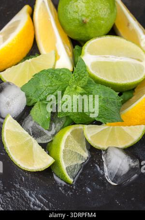 Lime, lemon, mint and ice cubes on black surface. The ingredients for making refreshing drinks, cocktails and lemonade. Selectiv Stock Photo