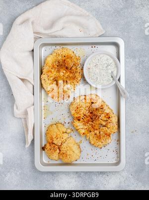 Baked cauliflower steaks with herbs and spices on a baking sheet on a gray concrete background. Mayonnaise sauce with dill, pars Stock Photo
