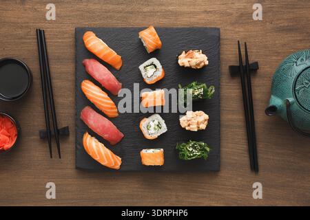 Sushi Served on a Black Platter With Chopsticks and Tea on a Wooden Table Stock Photo