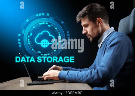 Man sits at desk using laptop for data storage tasks in modern workspace setting Stock Photo