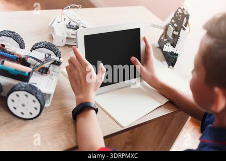 Child Using Tablet to Control Robot Car in Indoor Space With Toy Robots Around Stock Photo
