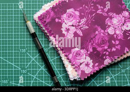 Fabric patchwork quilting patterned quilting squares on a green cutting mat with a craft knife background backdrop. Stock Photo