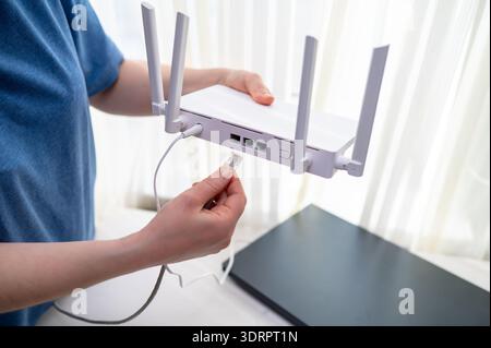 Close-up of a person in a blue shirt connecting a network cable into a wireless router with antennas. Concept of high speed internet setup, remote wor Stock Photo